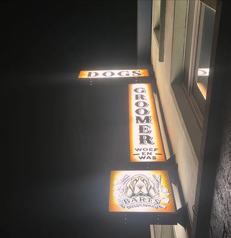 Het verlichte uithangbord van Dogs Groomer Bart bij avond